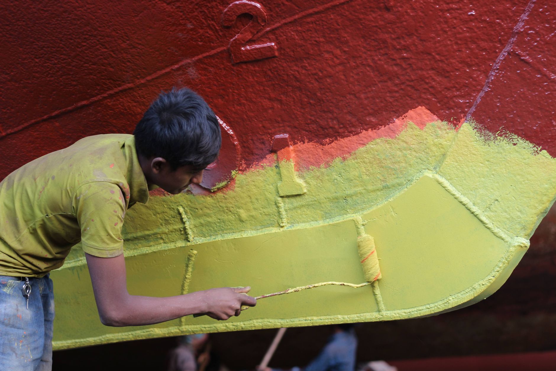 Man applying colorful paint to ship hull, blending red and green hues with precision. — Eco-Friendly Solutions Through Effici