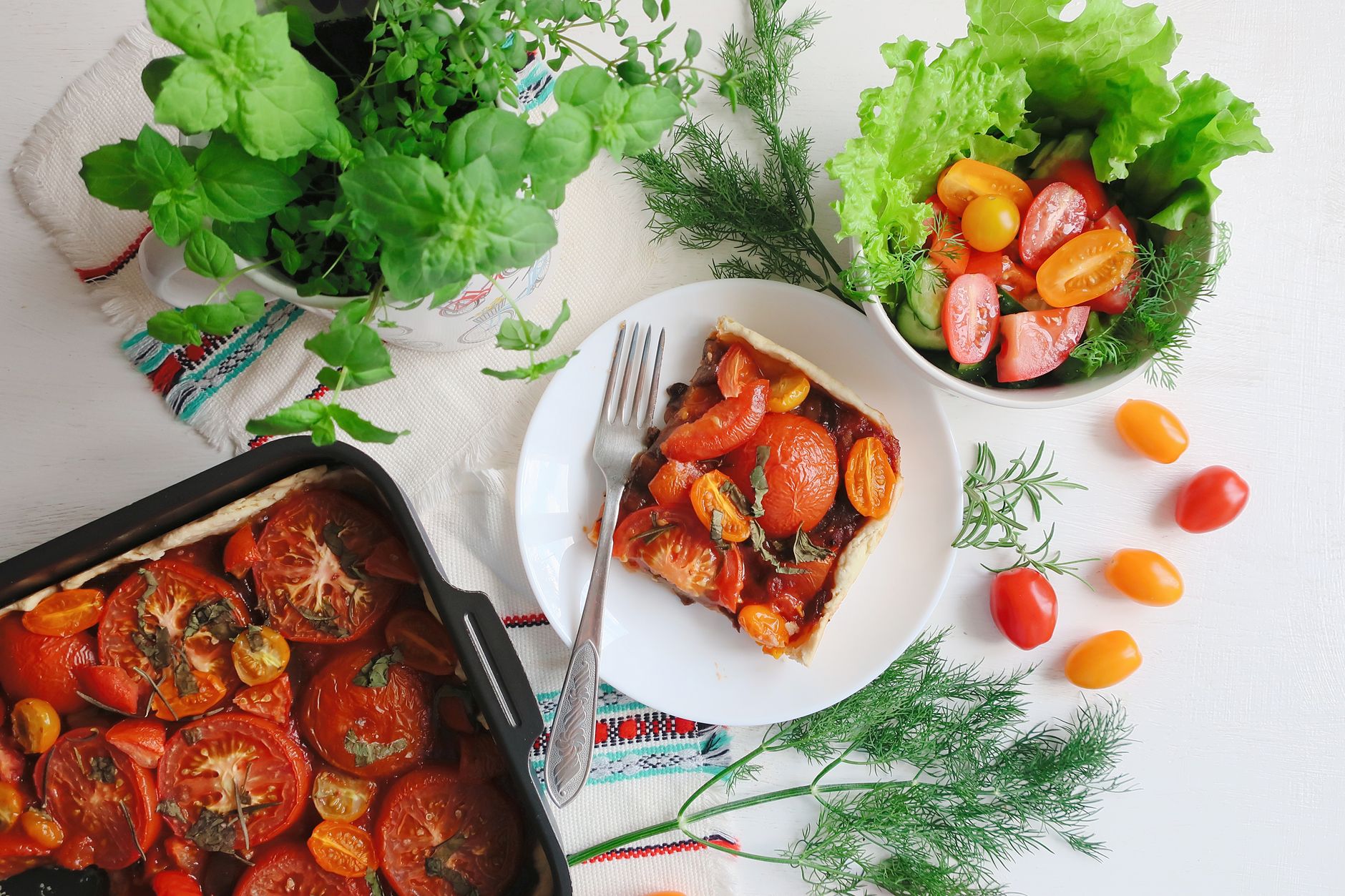 Top view of a vibrant tomato tart paired perfectly with a fresh salad and herbs. — Know More About The Best Selling Taste And
