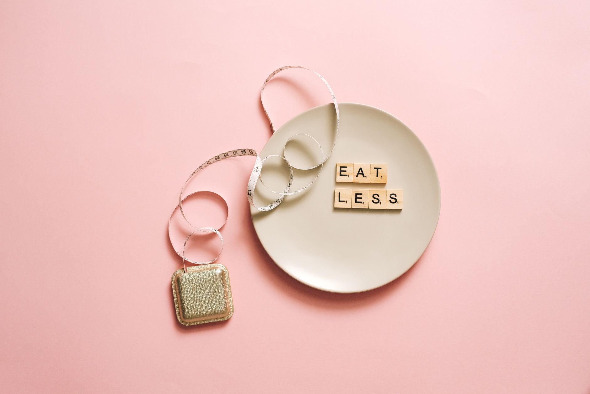 A motivational image featuring a plate with scrabble tiles spelling 'Eat Less' on a pink background. — Will a Gluten-free Die
